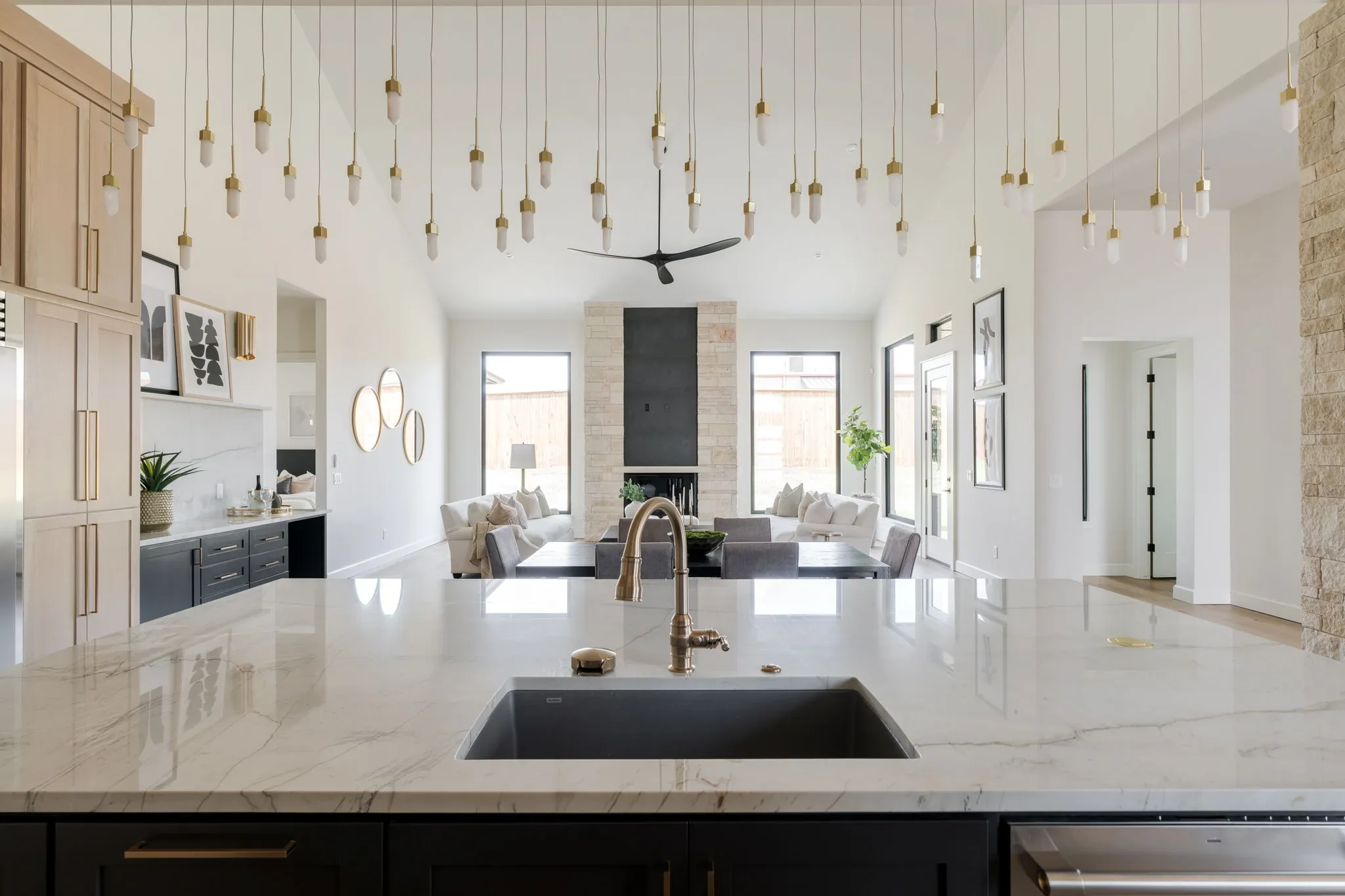 Kitchen island beneath brass pendants overlooking the double-height living room