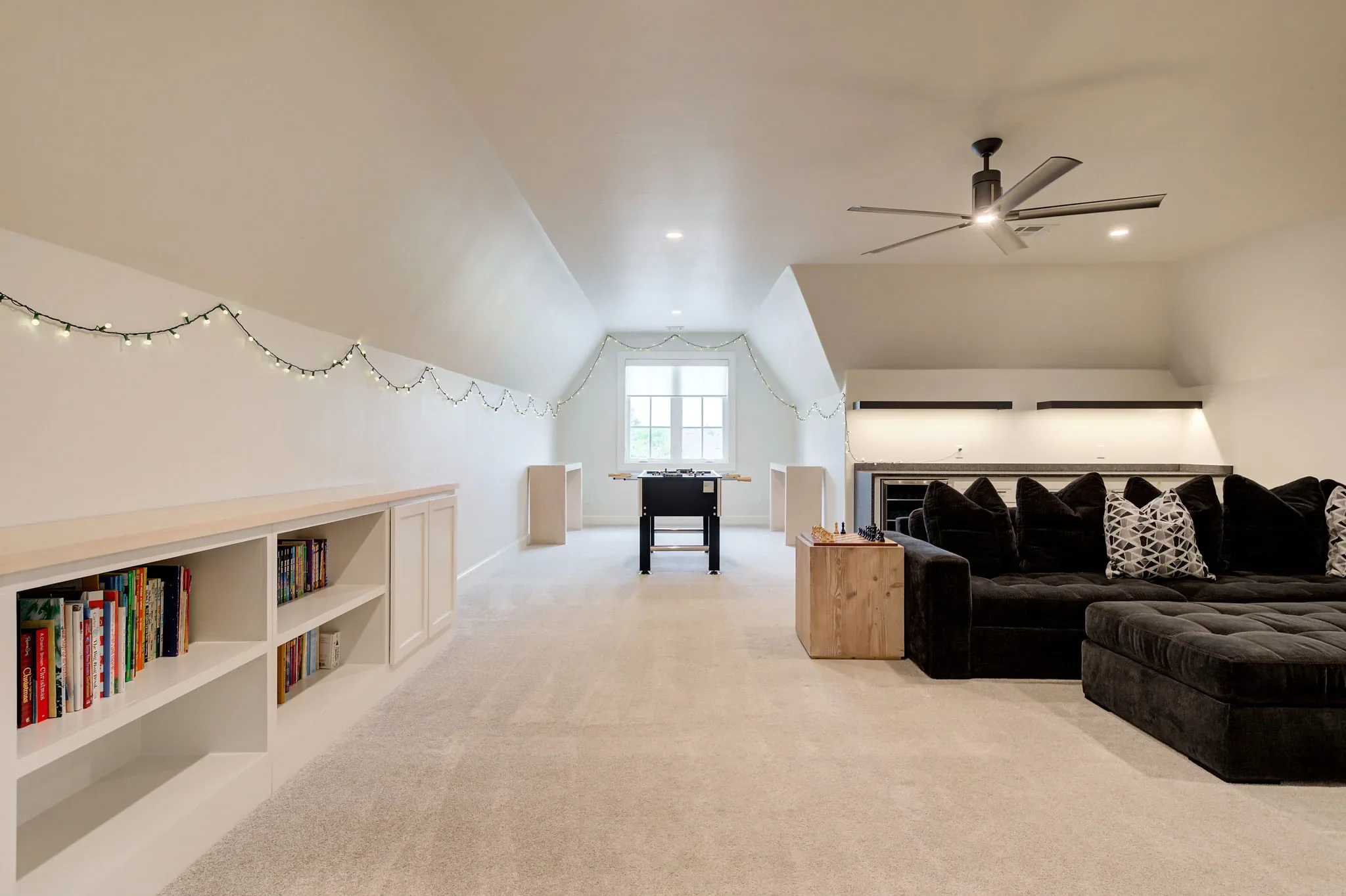 Upstairs bonus room with built-in bookshelves, sectional, and foosball table