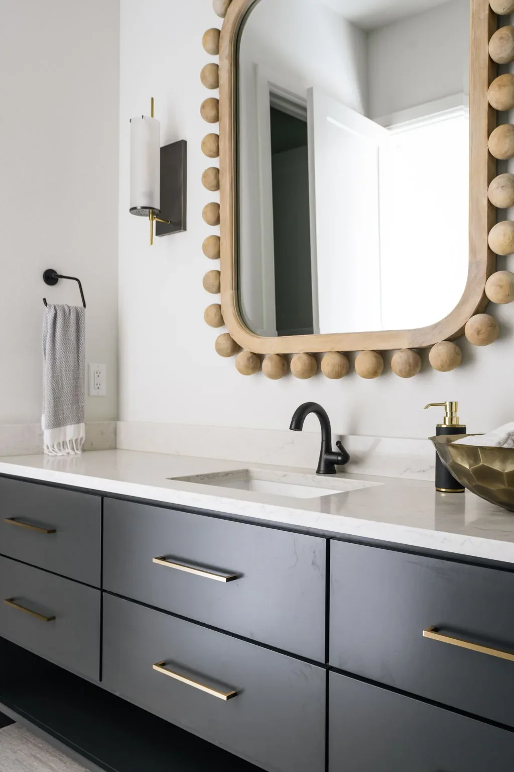 Charcoal bathroom vanity with brass hardware and a beaded wood mirror