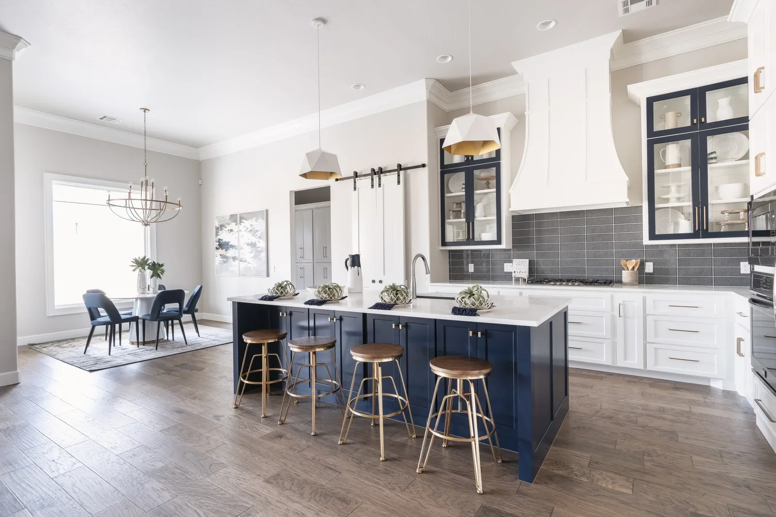 White kitchen with navy island, black backsplash, and gold pendants