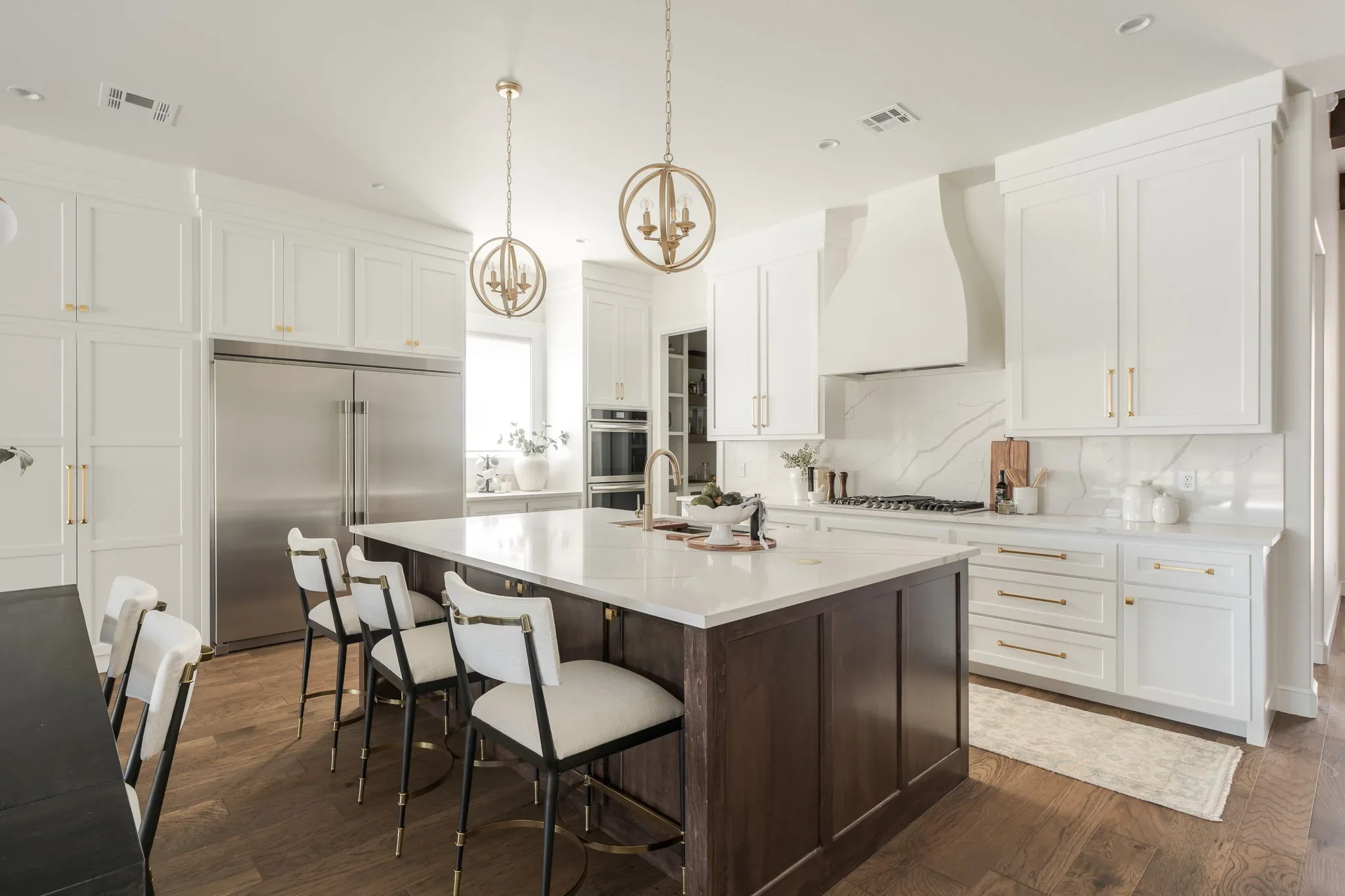 White kitchen with a dark wood island and brass pendant lights