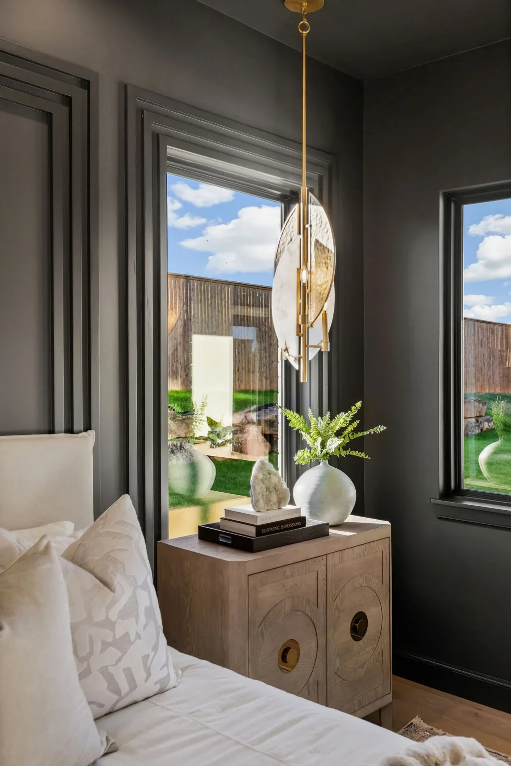 Black-paneled primary bedroom with brass pendant and garden views