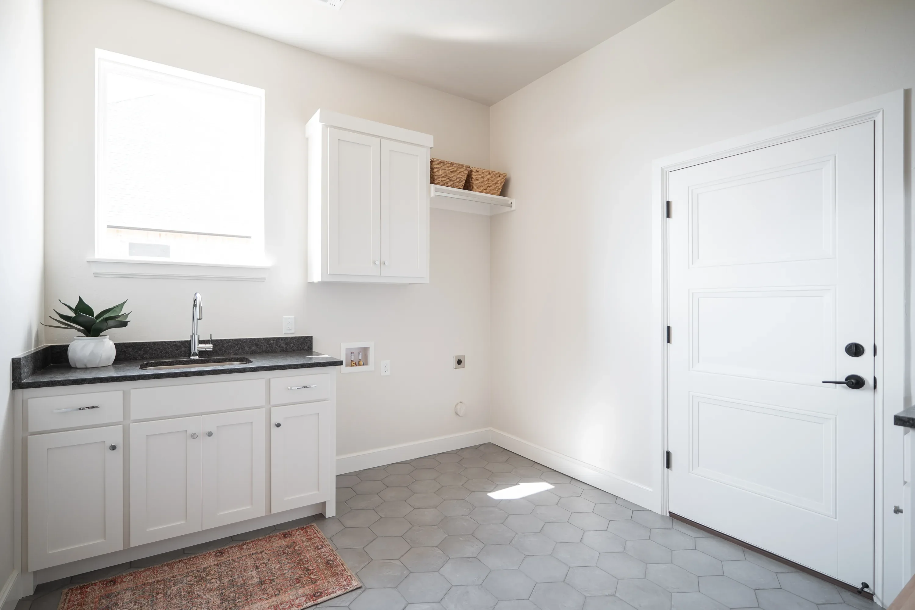 Laundry room with utility sink, white cabinetry, and hex tile