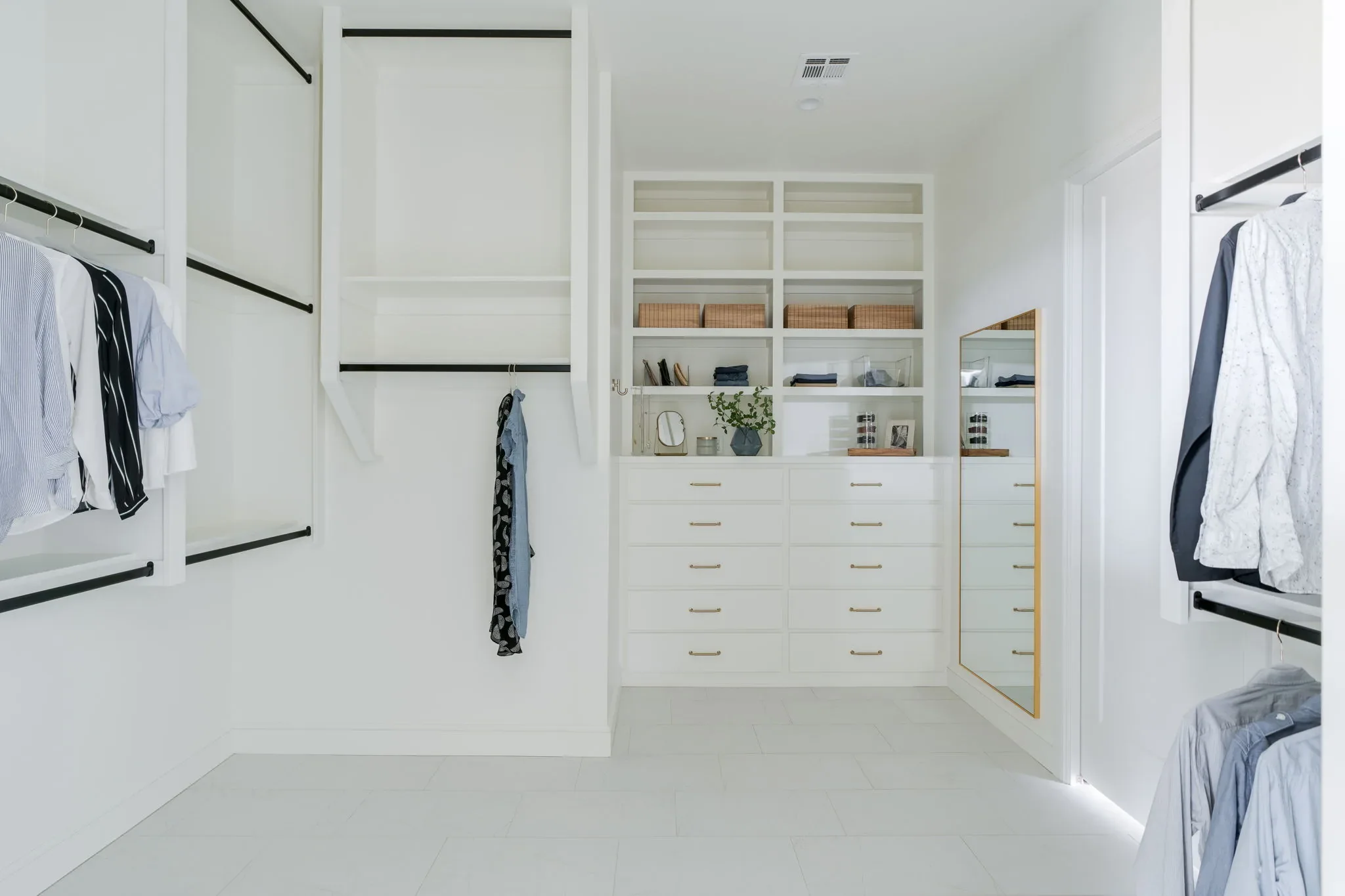 White walk-in closet with built-in drawers, shelving, and brass hardware