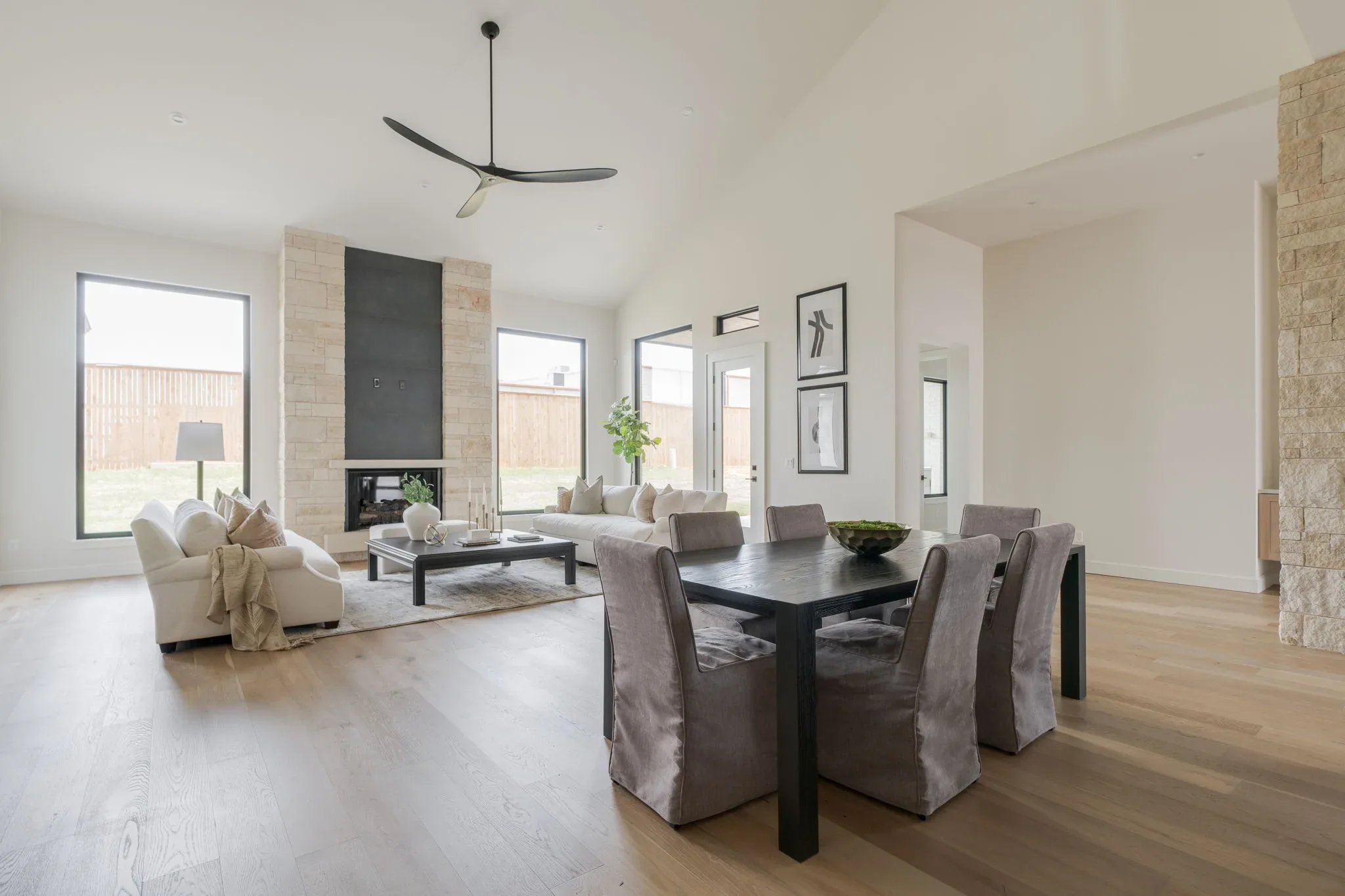 Open dining and living area with a stone fireplace and tall windows