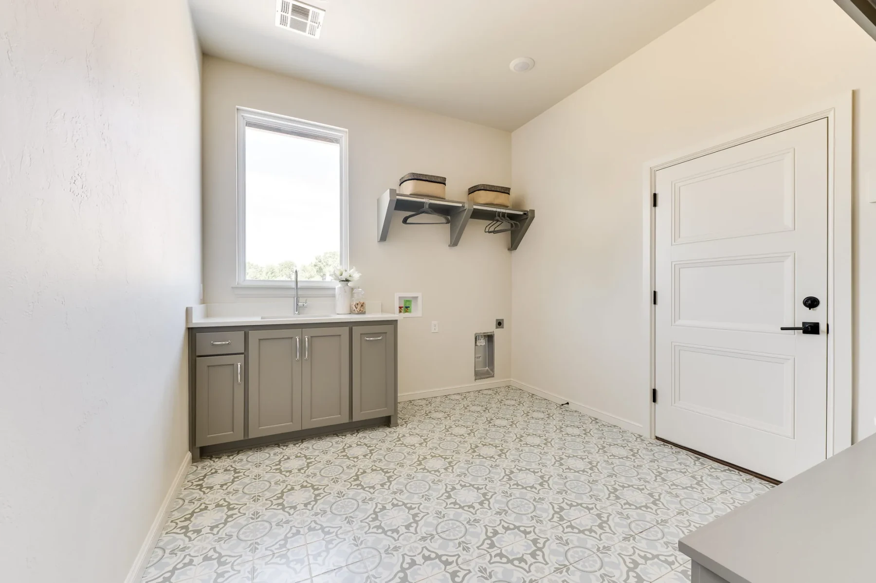 Laundry room with gray cabinetry and patterned tile flooring