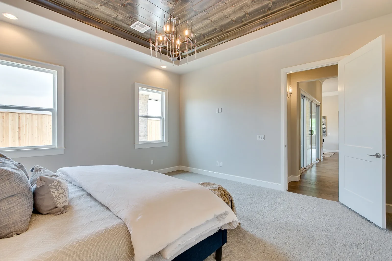 Primary bedroom with wood-paneled tray ceiling and modern chandelier