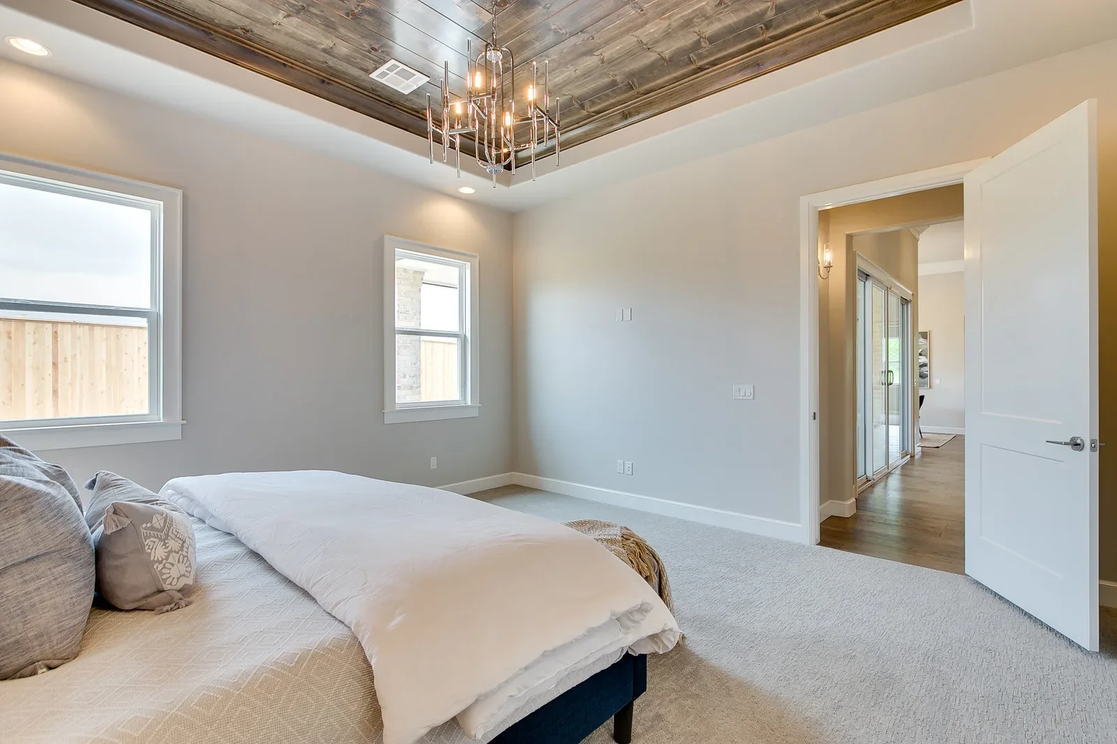 Primary bedroom with wood-paneled tray ceiling and modern chandelier