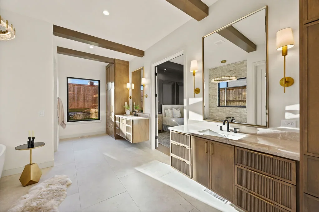 Primary bathroom with dual wood vanities and brass sconces