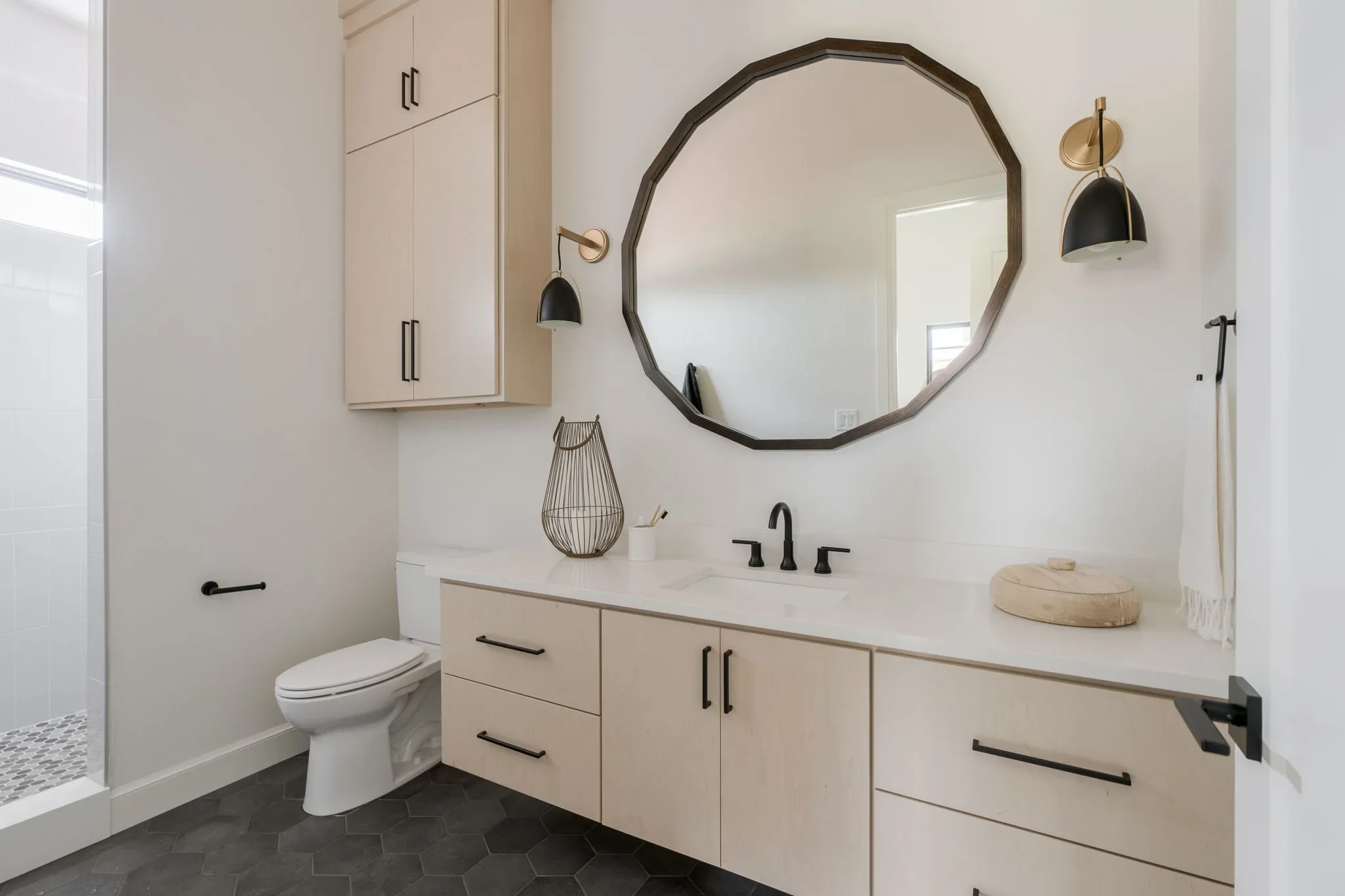 Bathroom with a light oak vanity, black hexagon tile, and walk-in shower