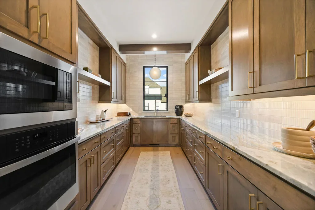 Galley prep kitchen with wood cabinets, sink, and stacked ovens