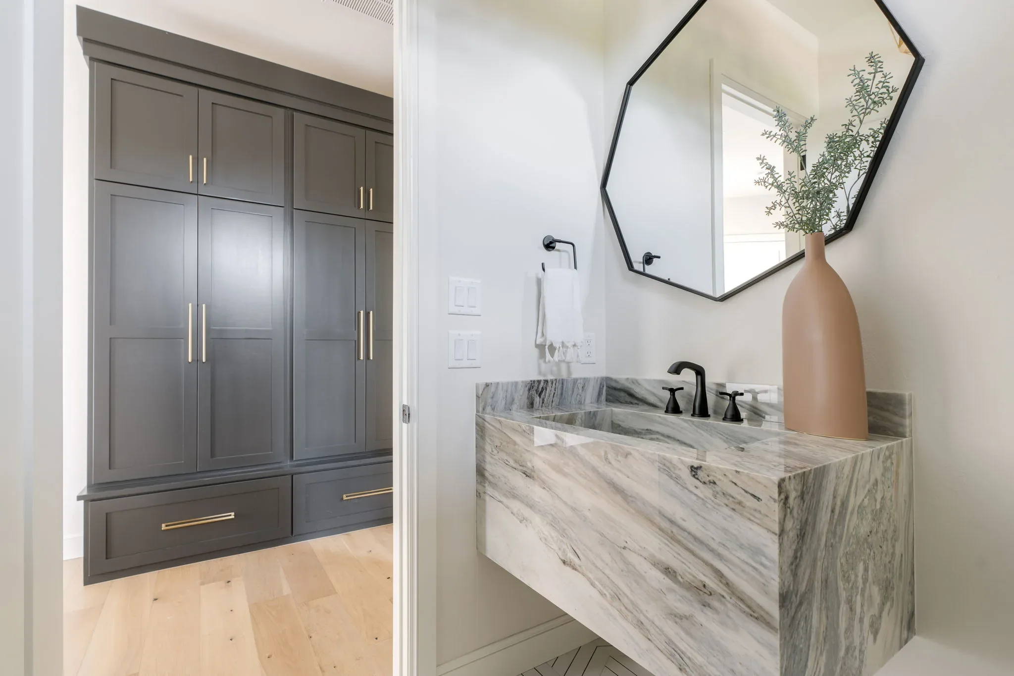 Charcoal mudroom built-ins beside a marble-wrapped powder room sink