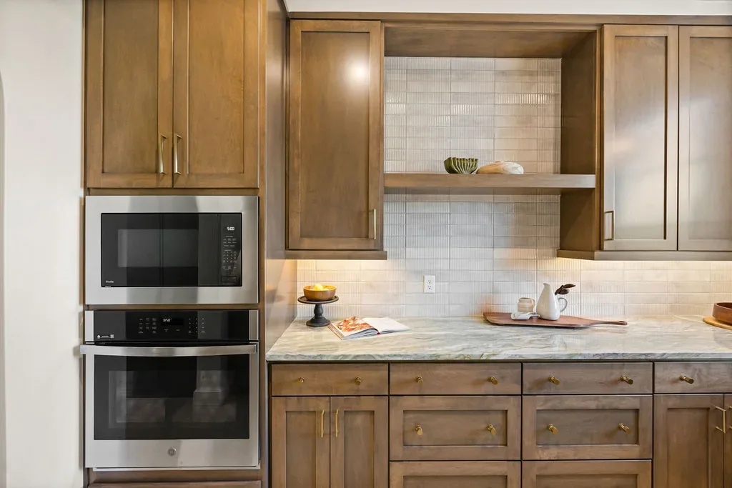 Wood kitchen cabinetry with stacked ovens and textured tile backsplash